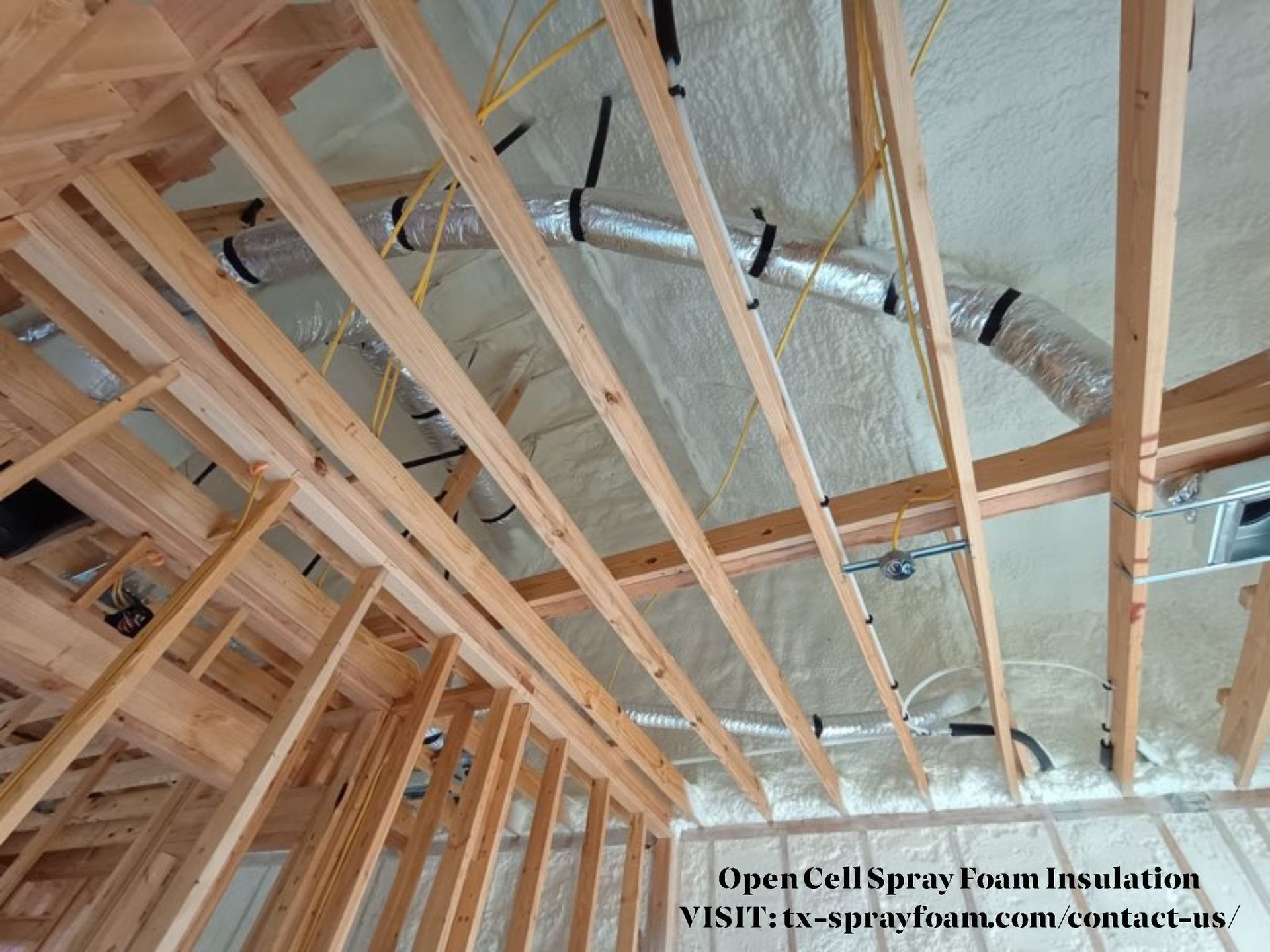 Open-cell spray foam insulation in a new home's rafters, with ductwork and electrical wiring.