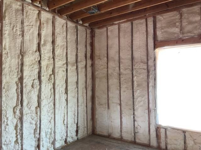 Interior view of a room with spray foam insulation between studs. Light tan color. Window visible.