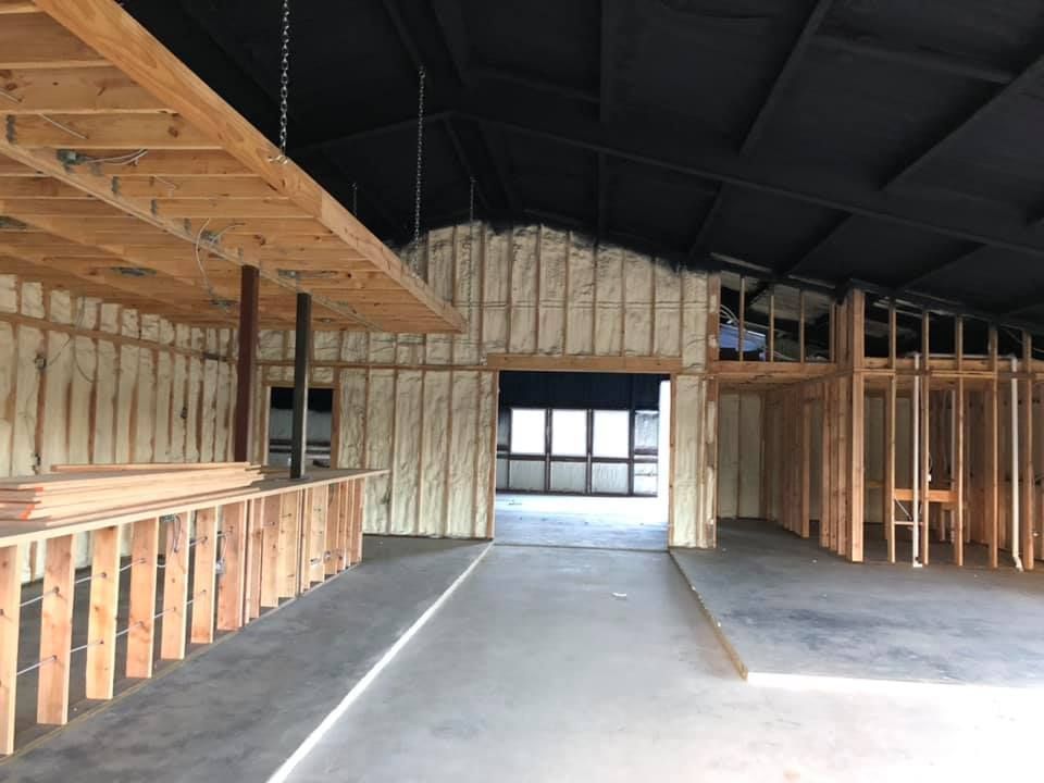 Interior construction view of a building with exposed wooden framing and insulation, concrete floor.