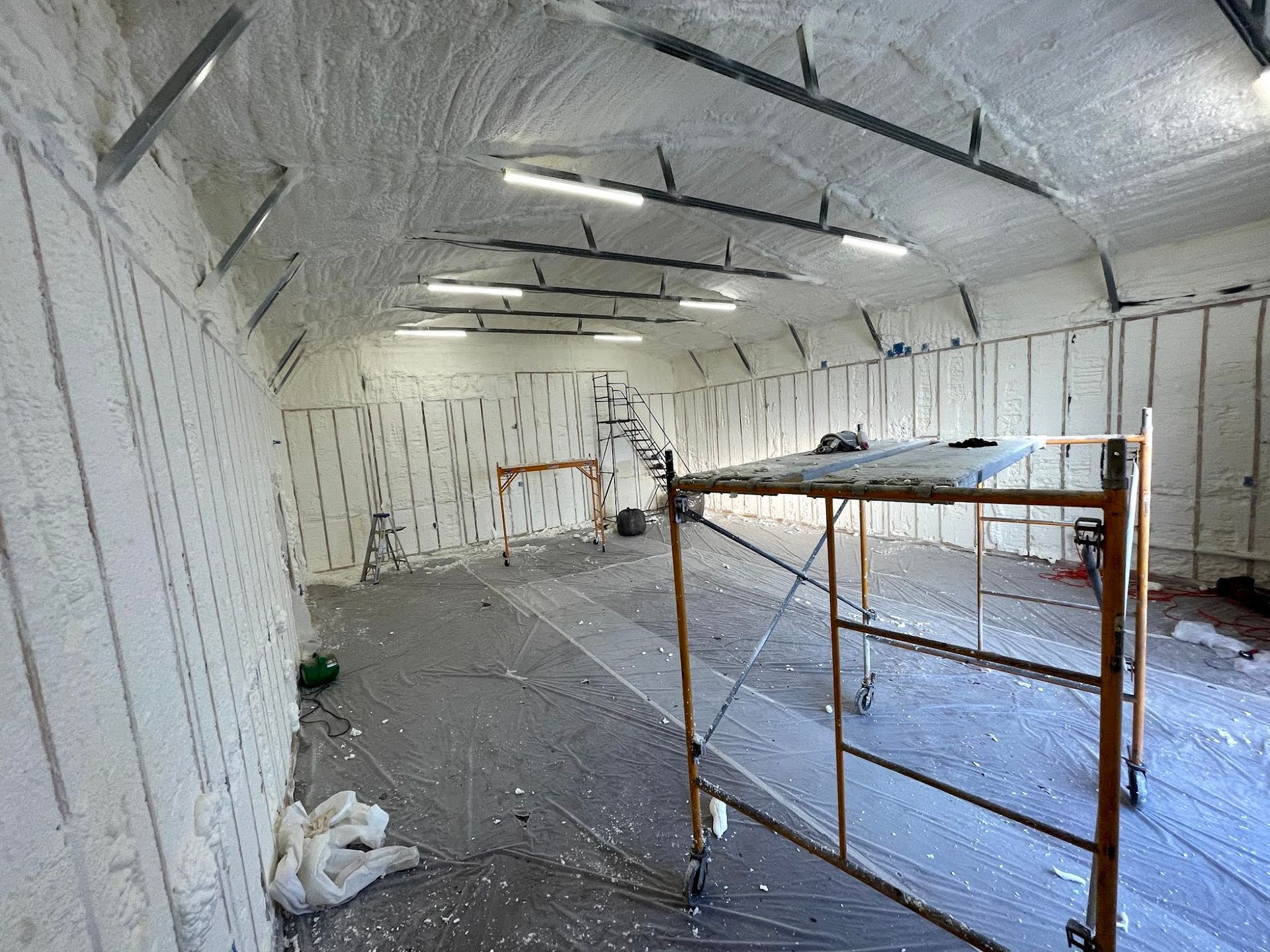 Interior of a building being insulated with spray foam. Scaffolding is in the foreground.