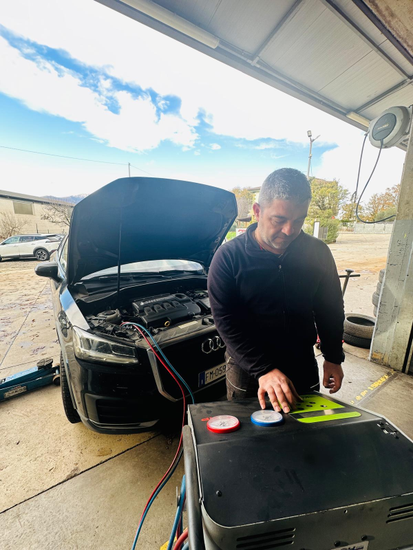 Un uomo sta lavorando su un'auto con il cofano aperto in un garage.