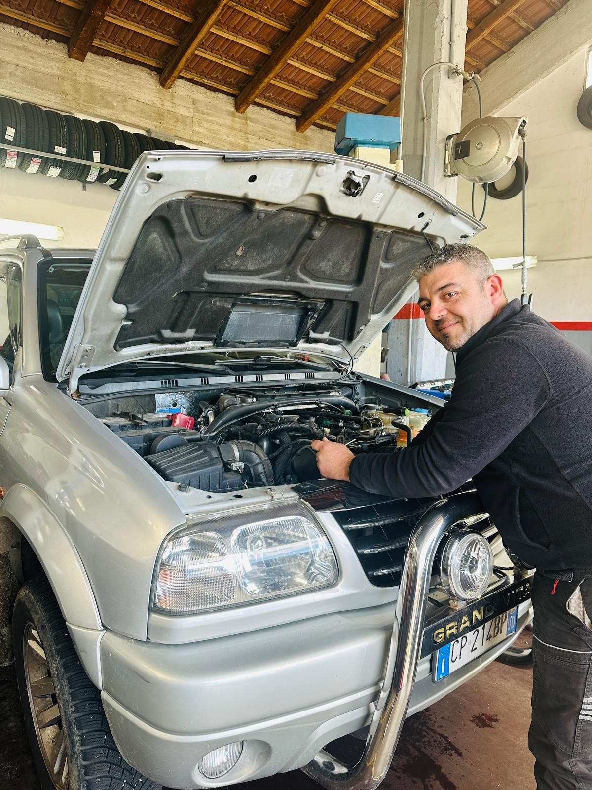Un uomo sta lavorando sul motore di un'auto con il cofano aperto.