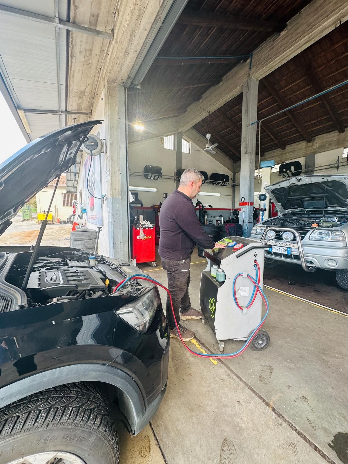 Un uomo sta lavorando su un'auto in un garage con il cofano alzato.