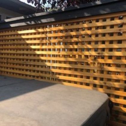 A wooden fence is surrounding a hot tub in a backyard.