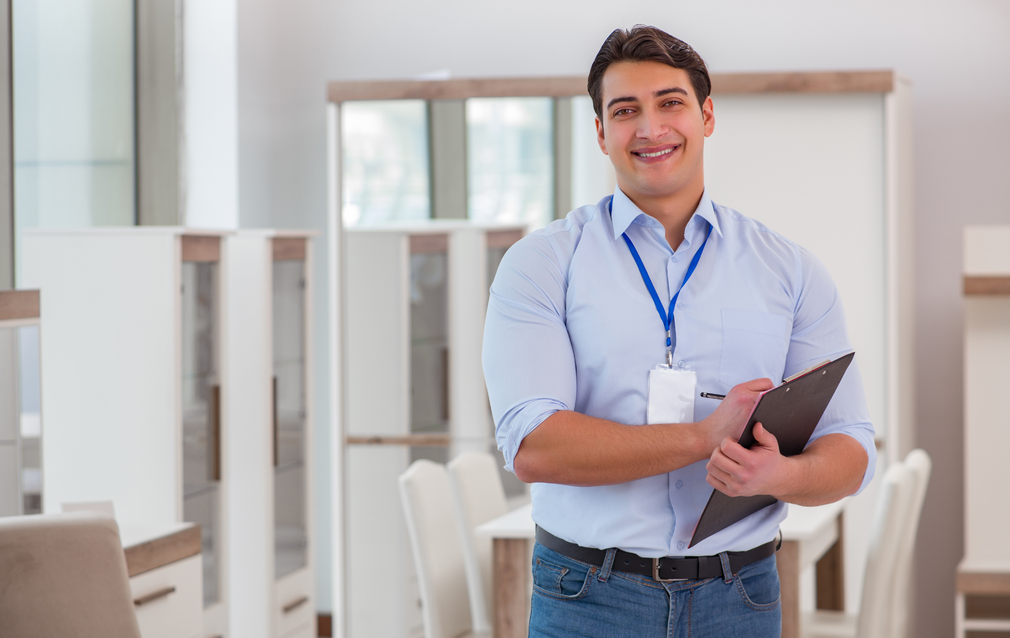 A man is holding a clipboard in a furniture store.