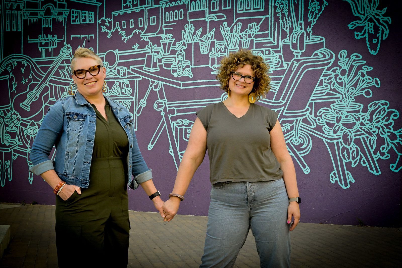 Two women holding hands in front of a purple wall