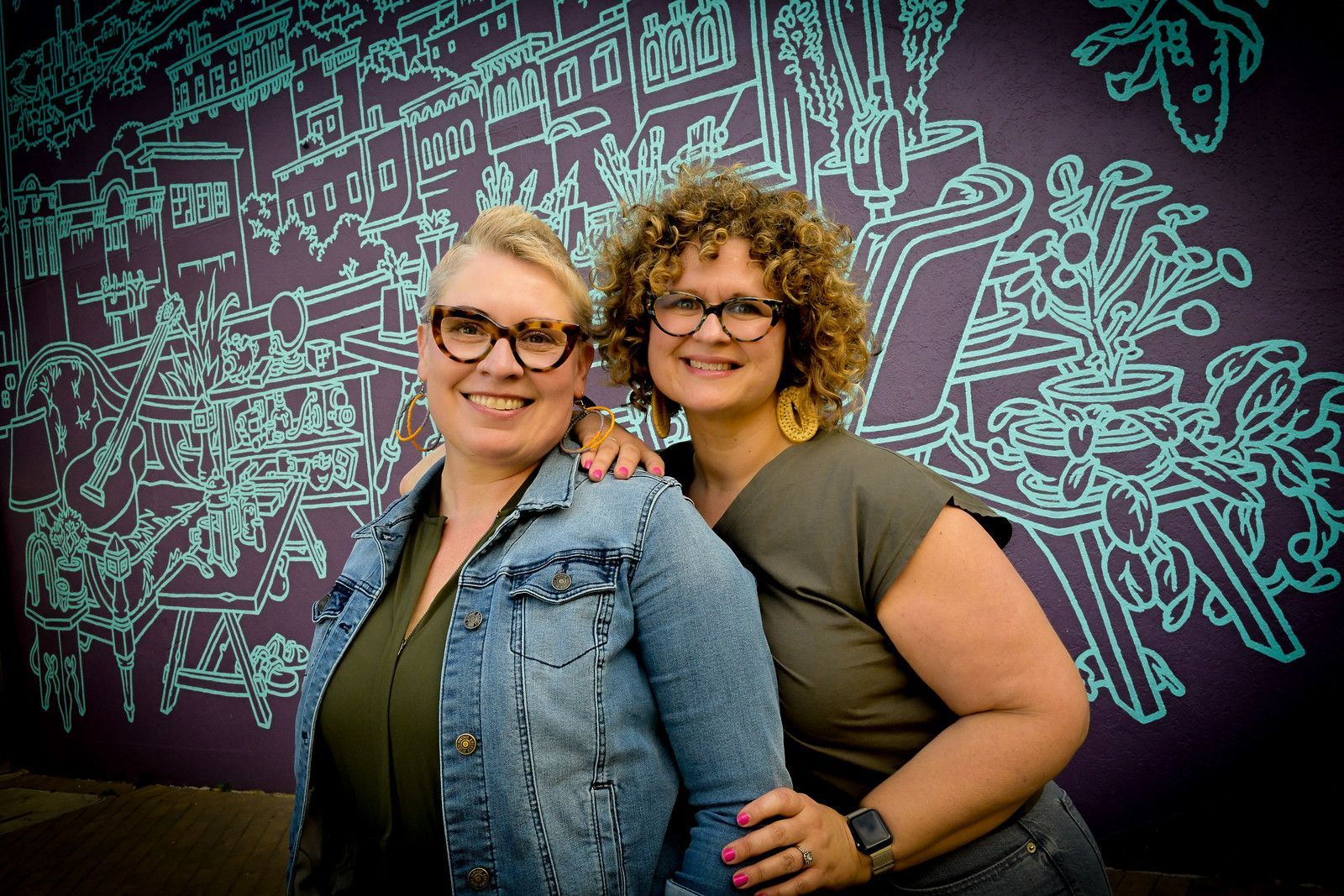 Two women are posing for a picture in front of a purple wall.