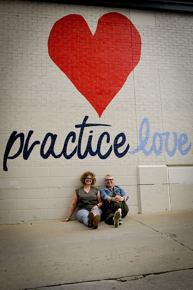 Two people are sitting in front of a wall that says practice love