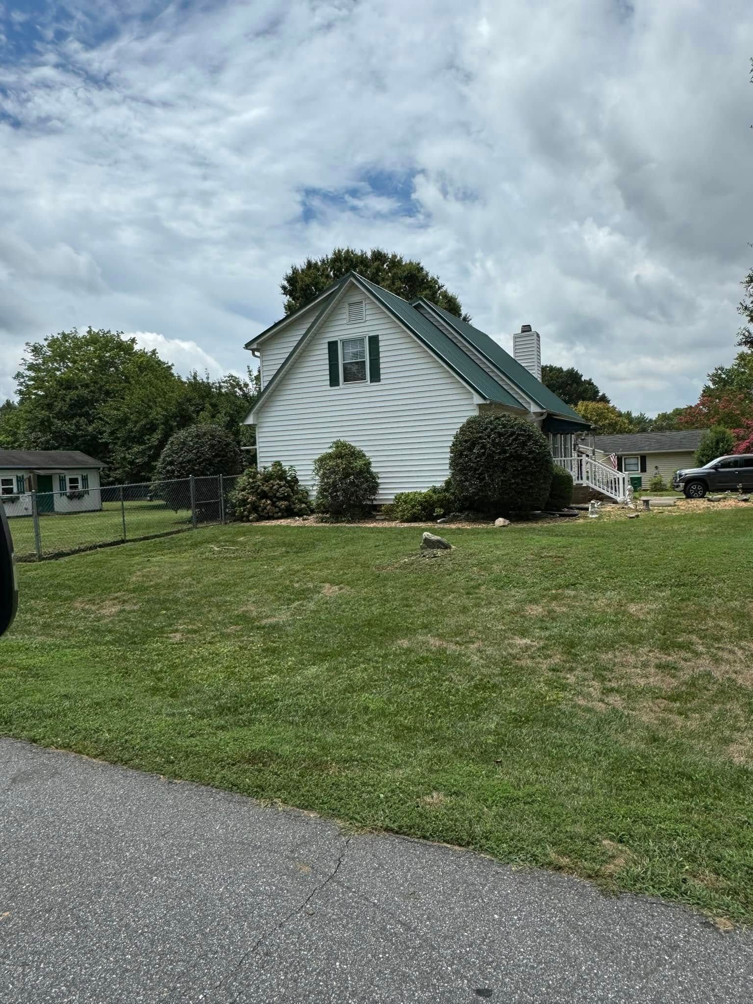 White house with green roof and shutters, set on a grassy lawn under a cloudy sky.