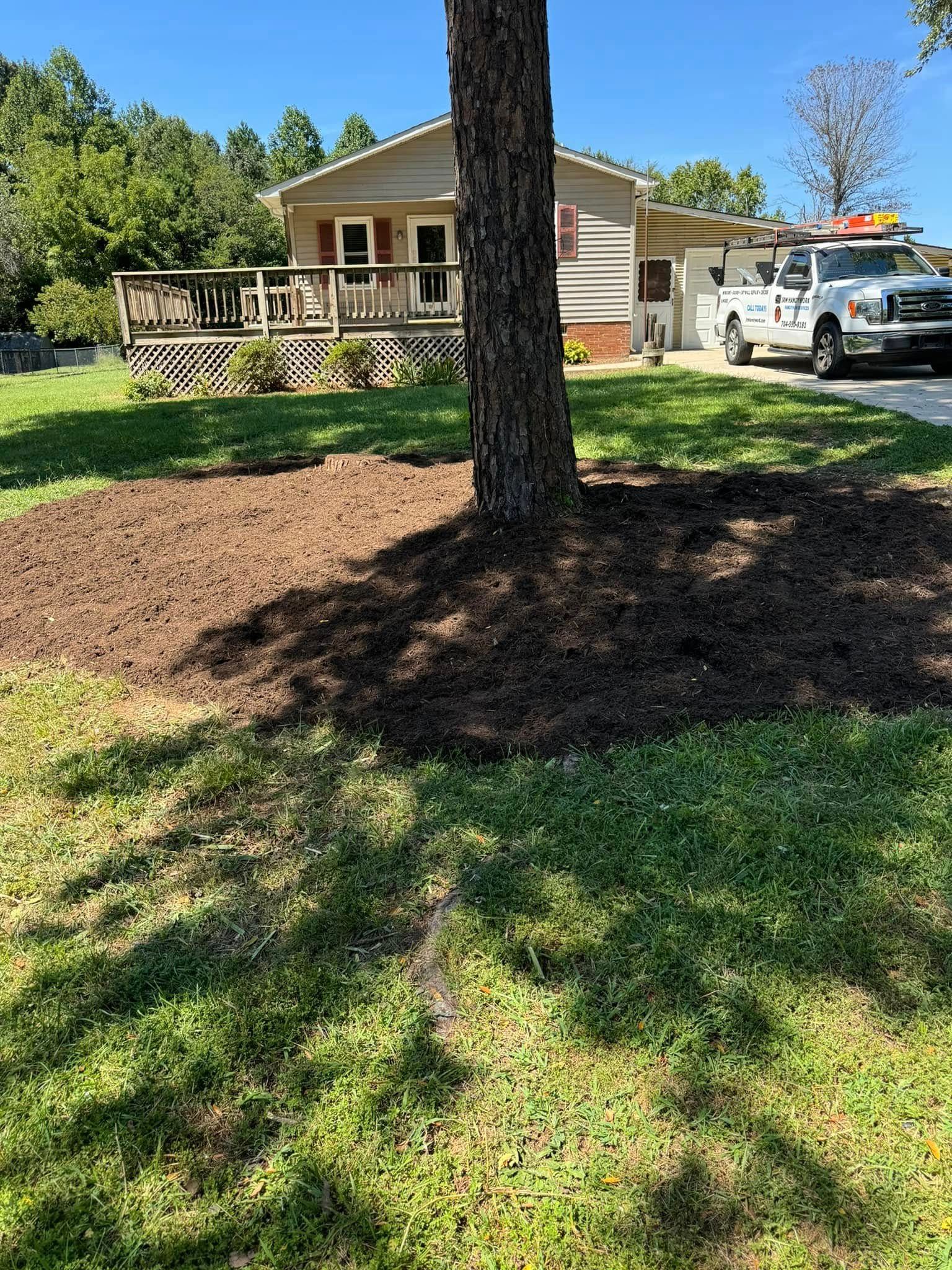 A tree surrounded by fresh mulch in front of a house and service truck on a sunny day. Green grass.