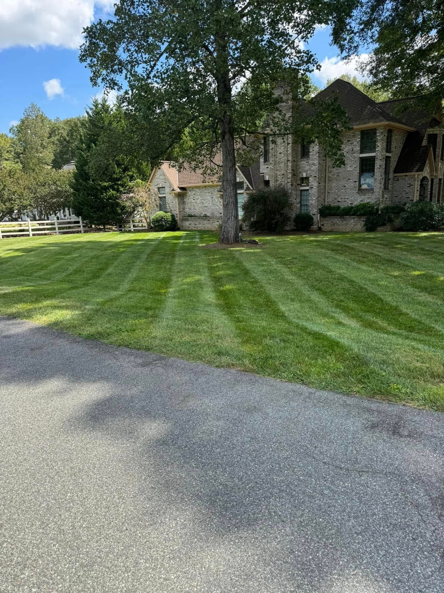 A freshly mowed lawn with striped patterns in front of a large brick house and mature trees on a sunny day.
