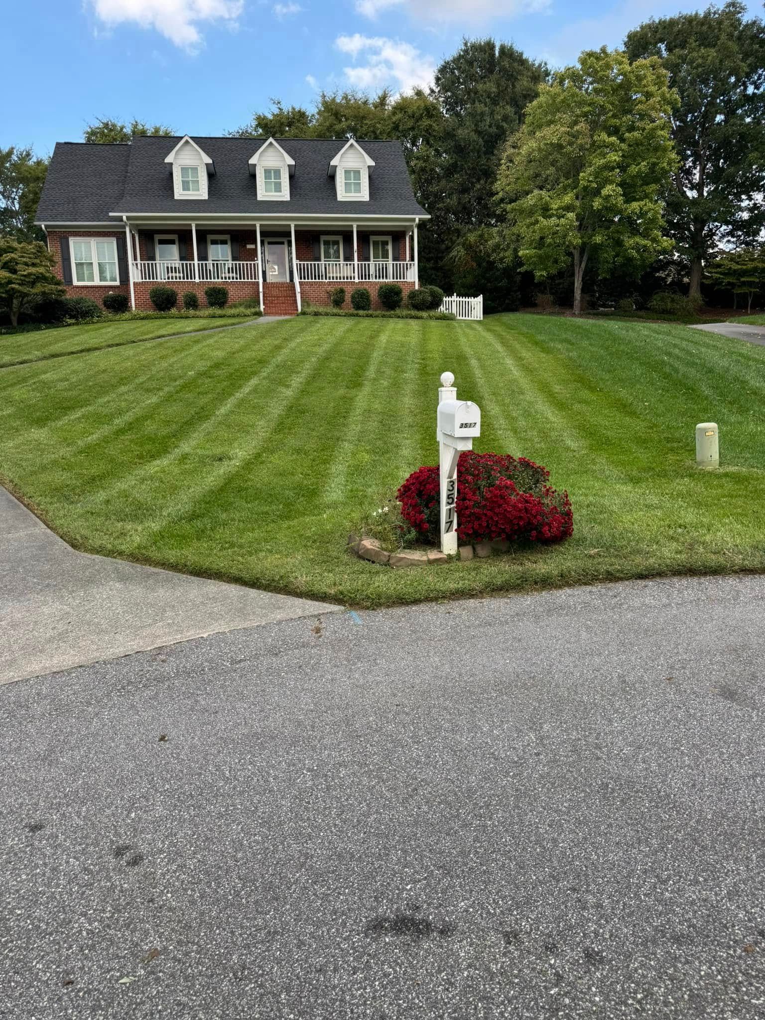 A house with a manicured lawn, mailbox, and dark driveway. The lawn has fresh, striped mowing pattern.