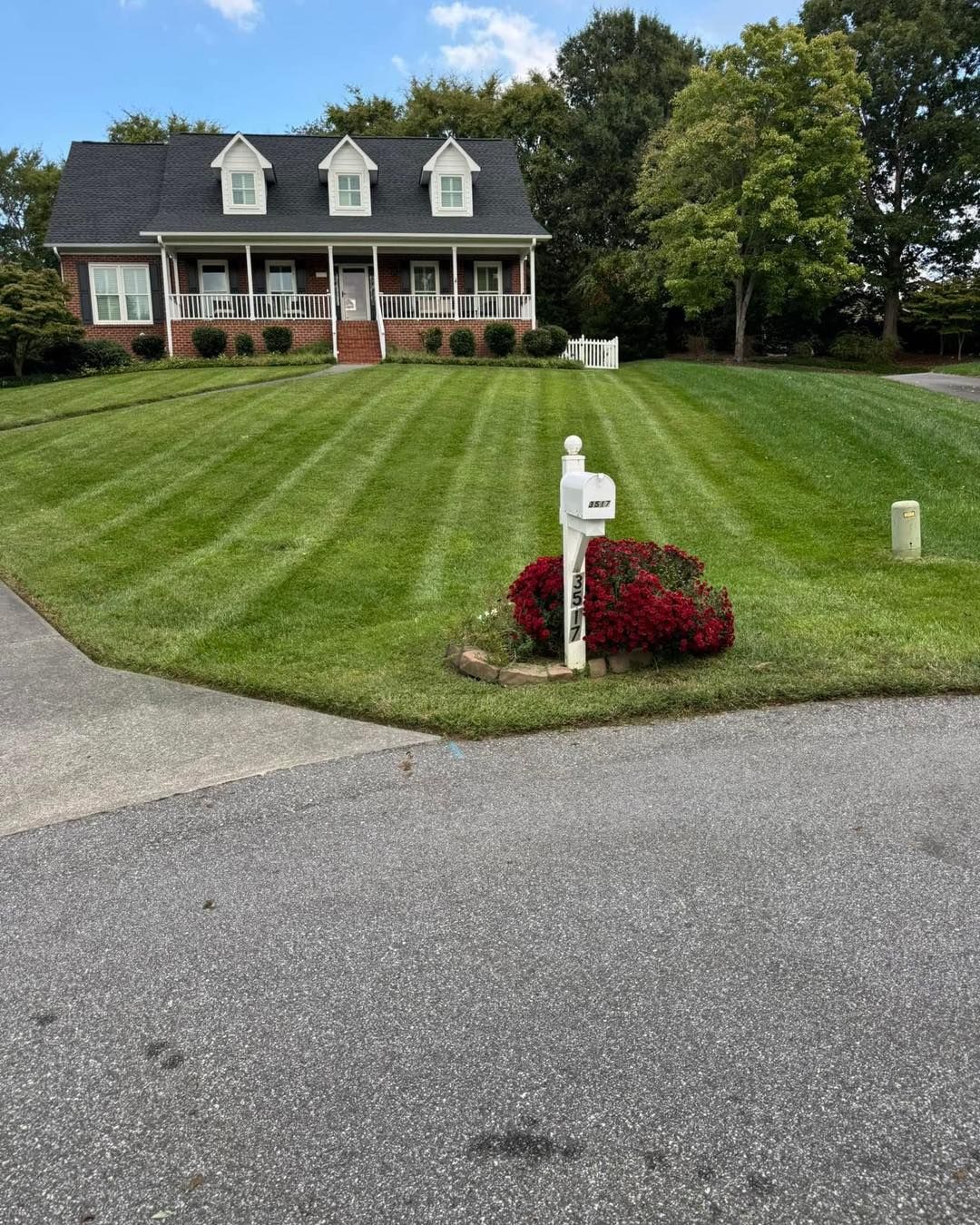 House with a manicured lawn, a mailbox, and vibrant red bushes. The lawn has neat mowing stripes.