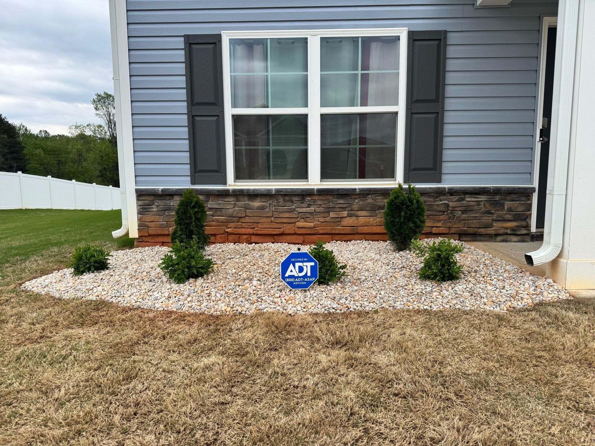 A house exterior with a rock garden, featuring blue siding, dark shutters, and an ADT security sign.