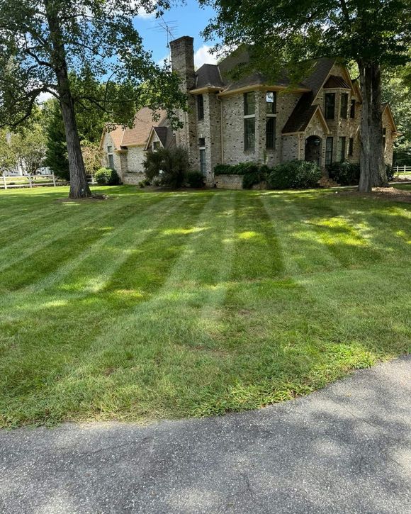A front yard with brown mulch flower beds, green bushes, and a light gray house with white pillars.
