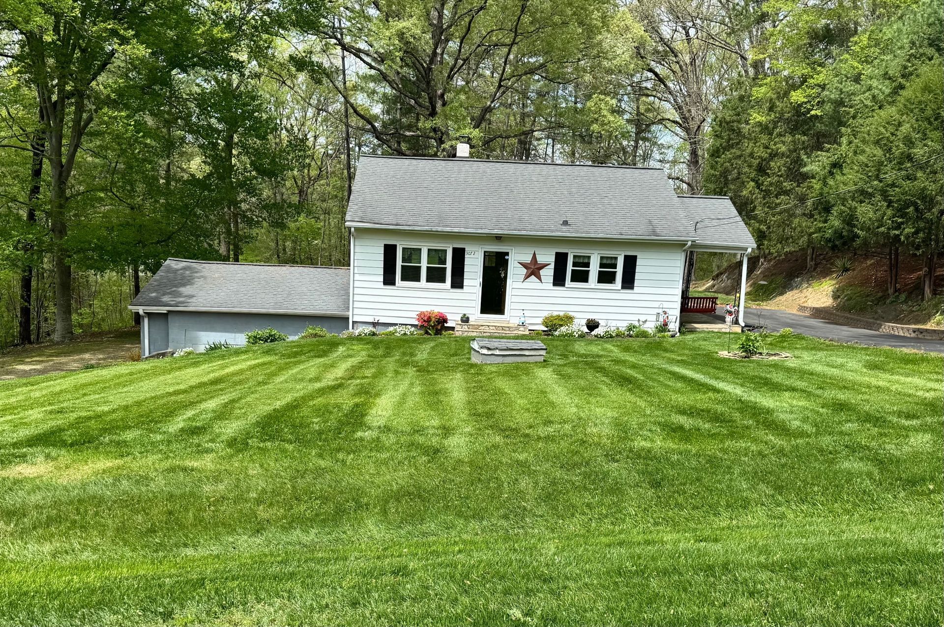 White house with a freshly mowed lawn, a star decoration, and trees in the background.