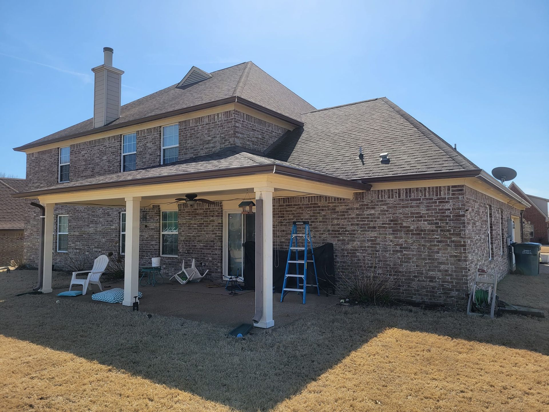A large brick house with a porch and a ladder in front of it.