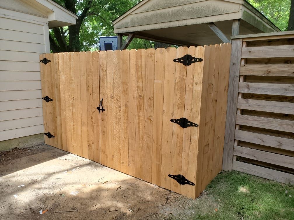 A wooden fence with black hinges is in front of a white house.