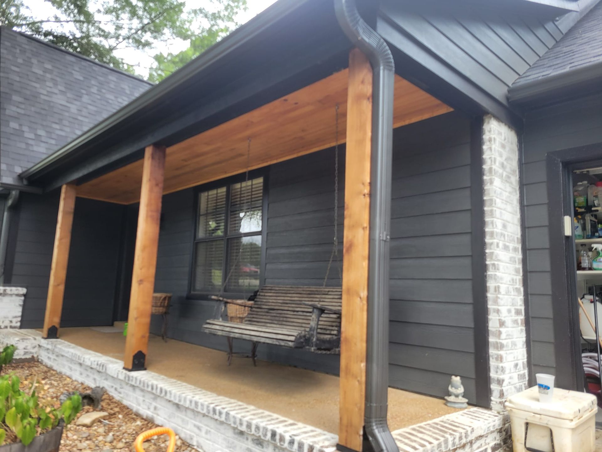 A black house with a porch and a swing on it.