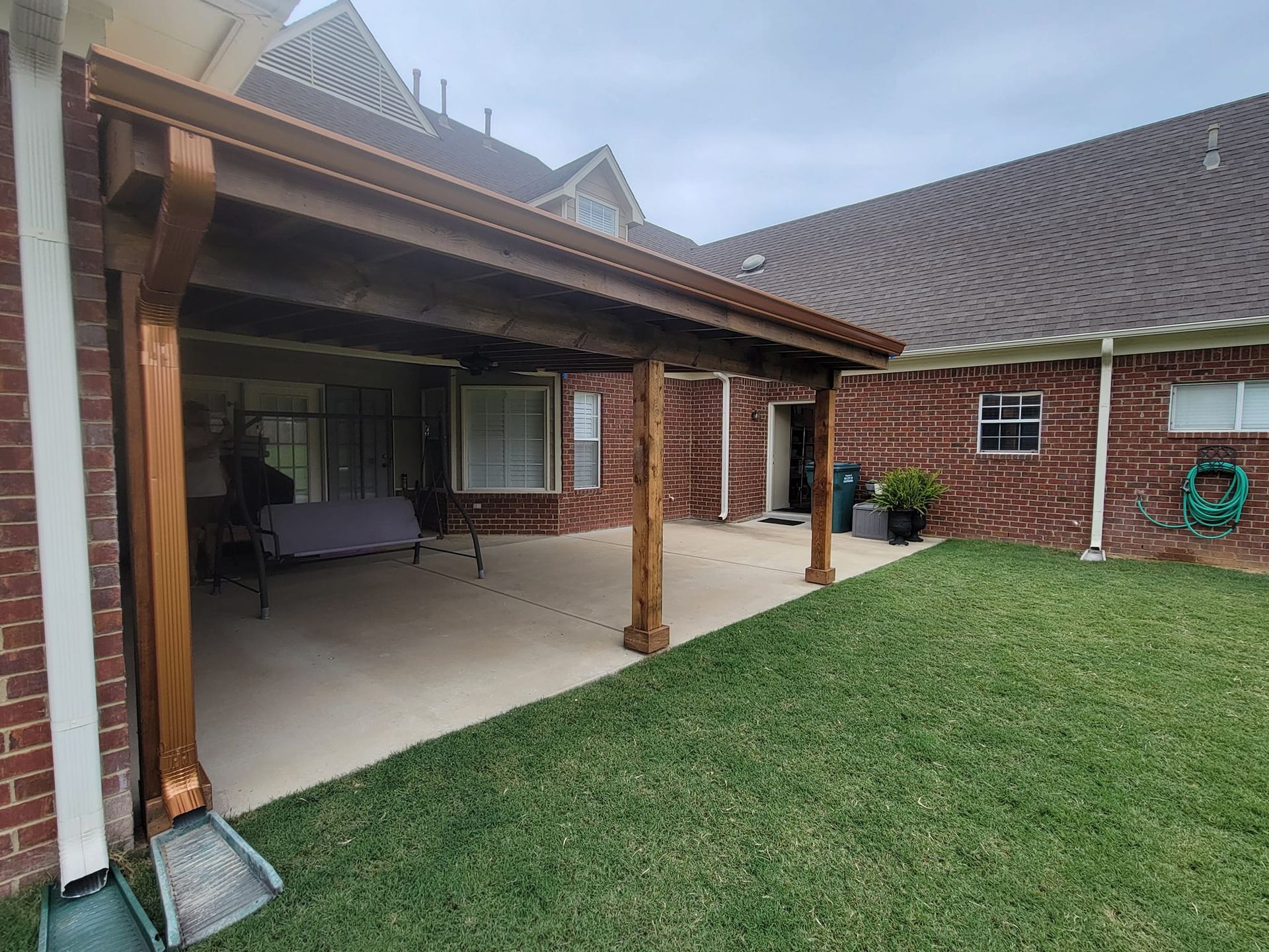 There is a covered patio in the backyard of a brick house.