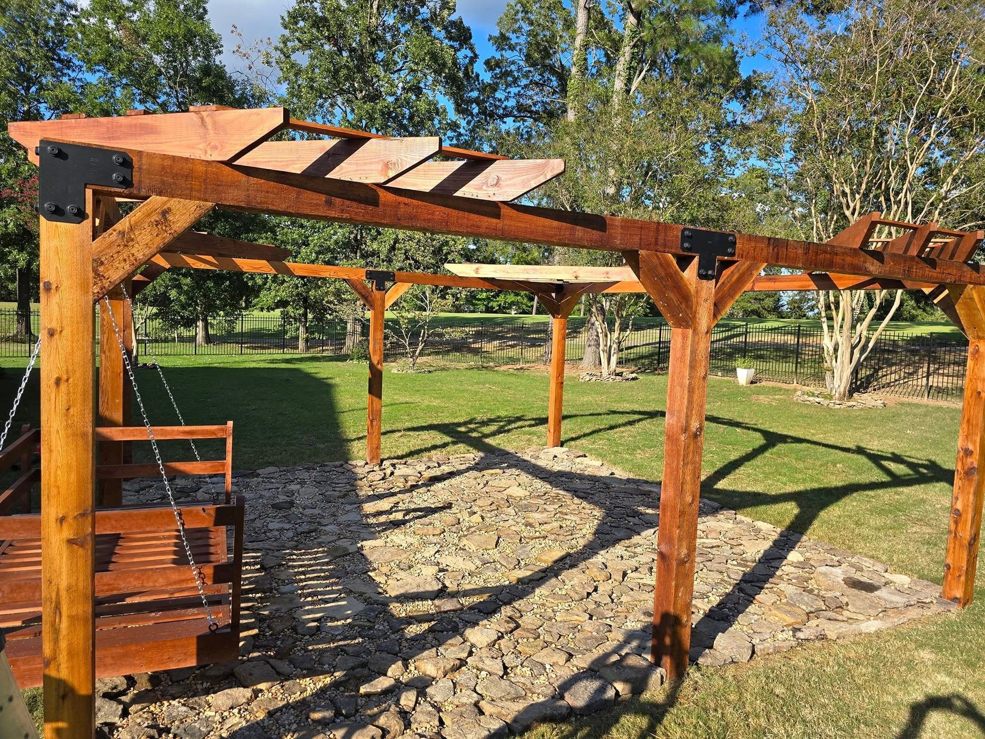 A wooden pergola with a swing underneath it in a yard.