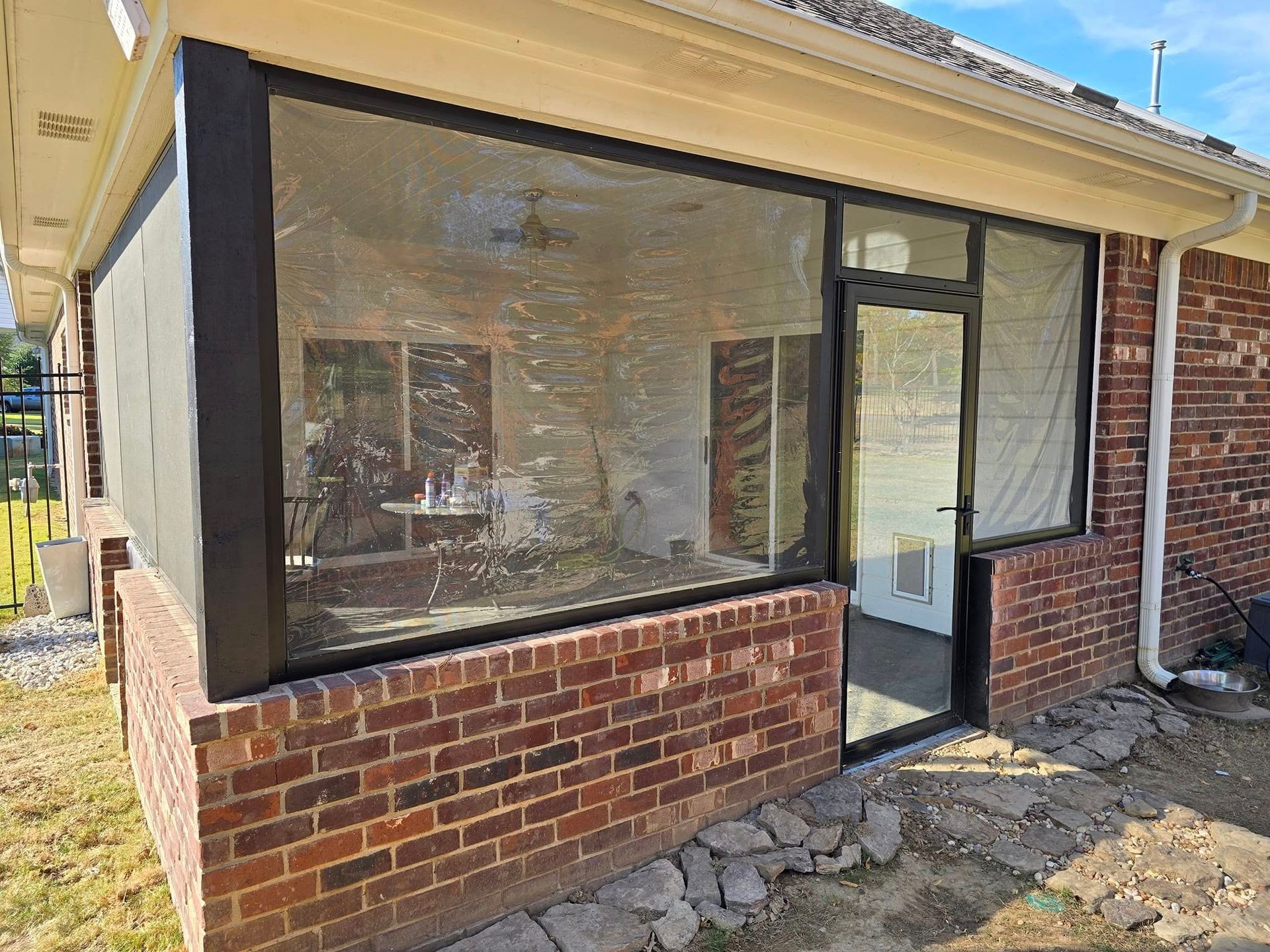 A screened in porch with a brick wall and a glass door.