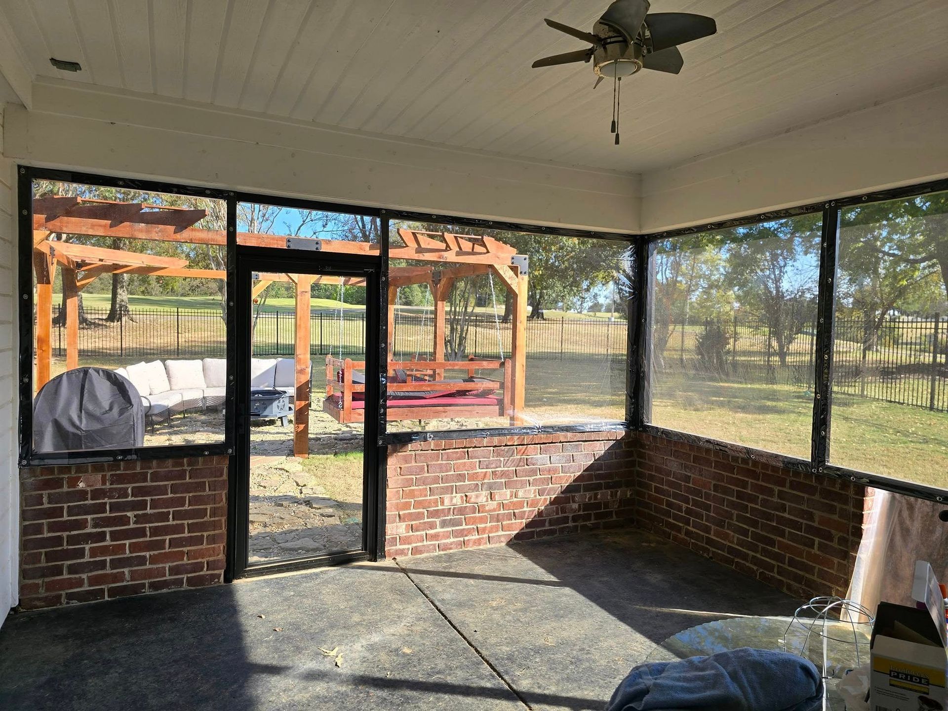 A screened in porch with a ceiling fan and a gazebo in the background.