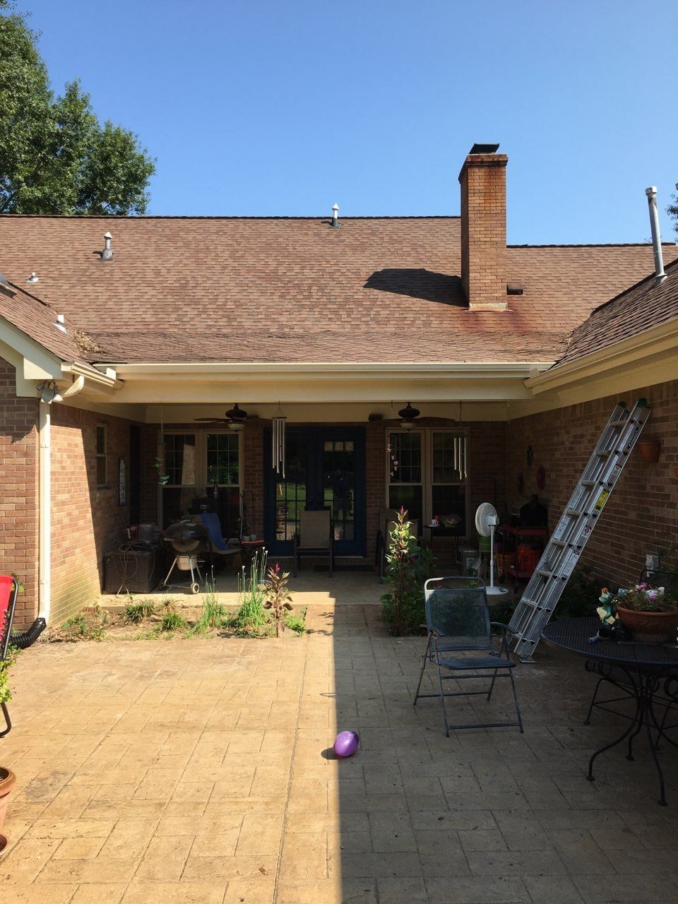 A brick house with a red roof and a patio in front of it.