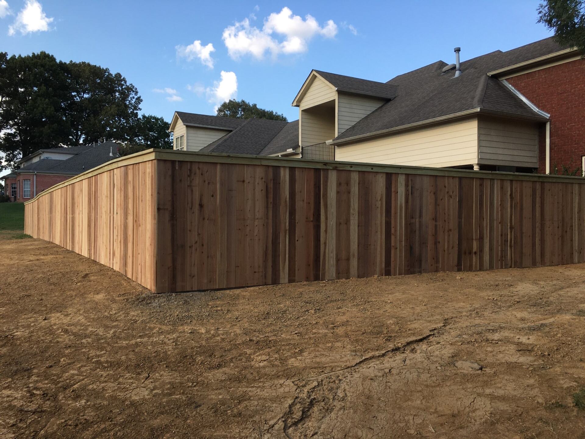 A wooden fence surrounds a dirt field in front of a house.