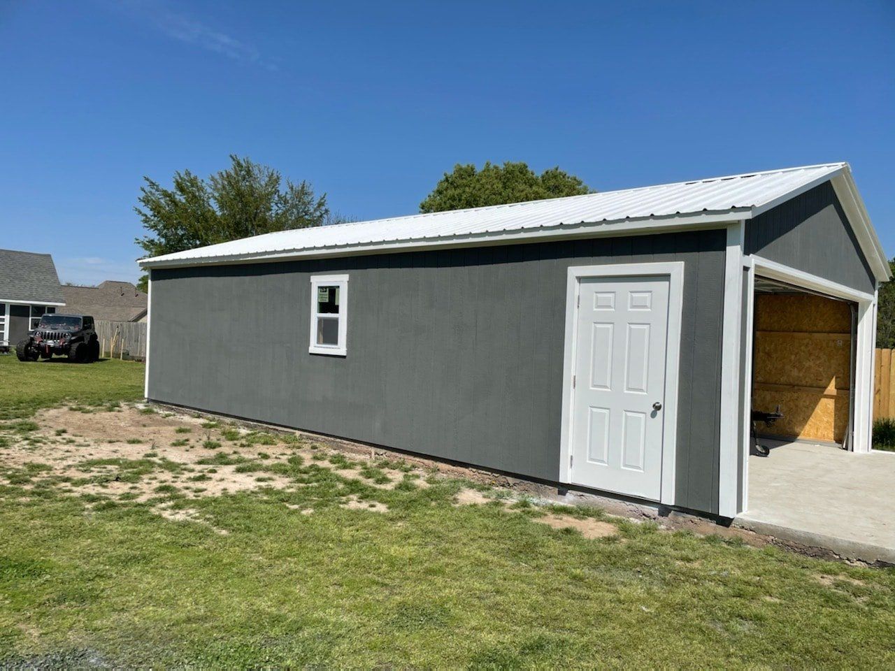 A gray garage with a white roof is sitting in the middle of a grassy field.