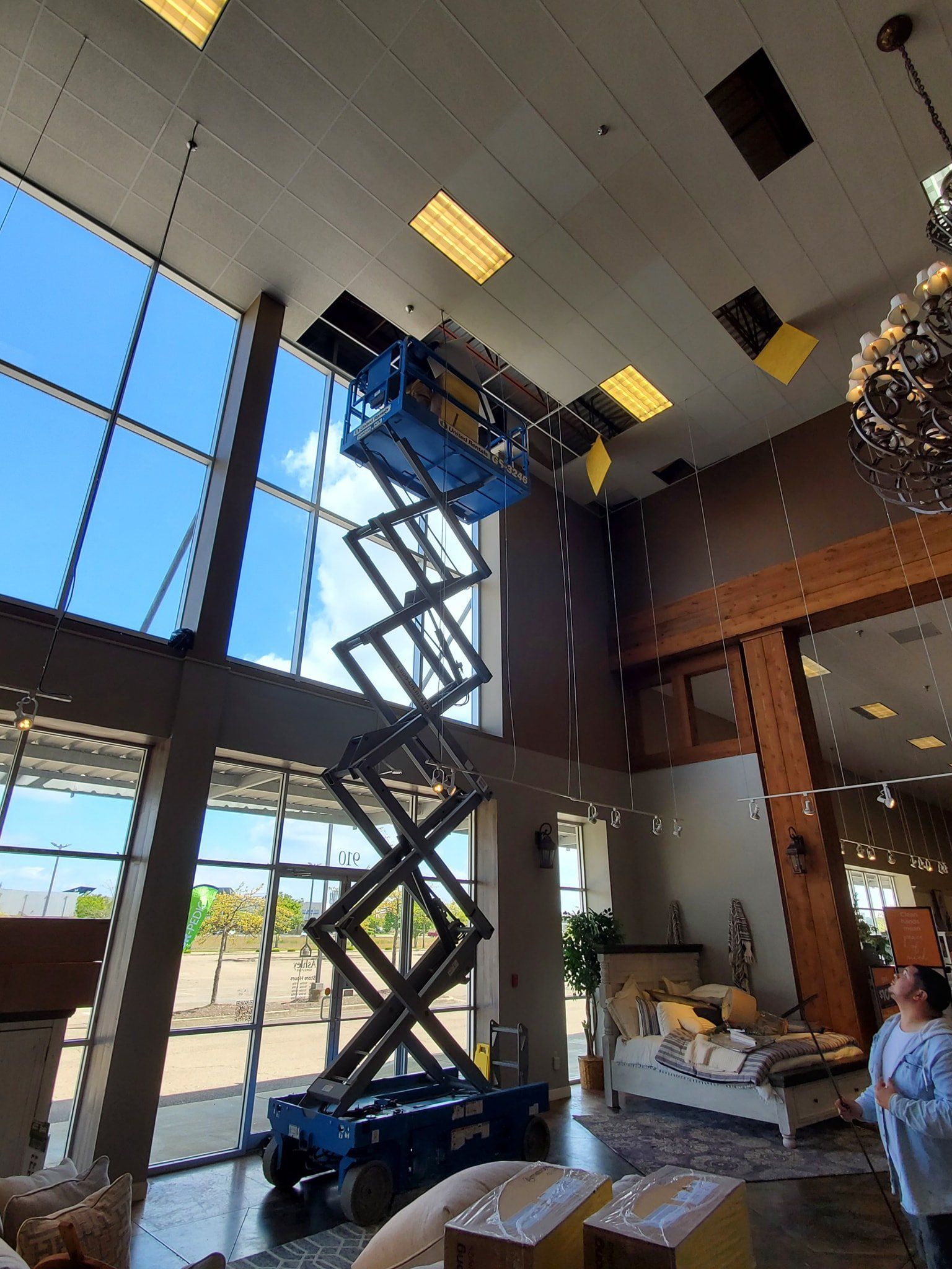 A man is standing in a living room looking up at a scissor lift.
