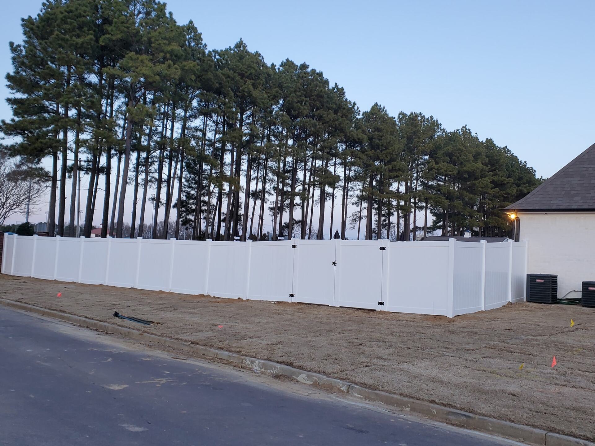A white fence is surrounded by trees in front of a house.