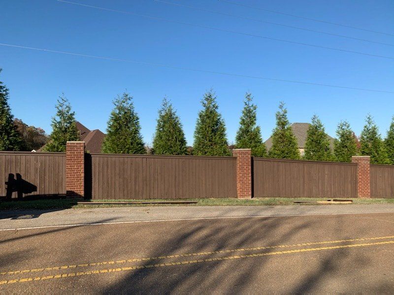 A wooden fence surrounds a driveway with trees in the background.