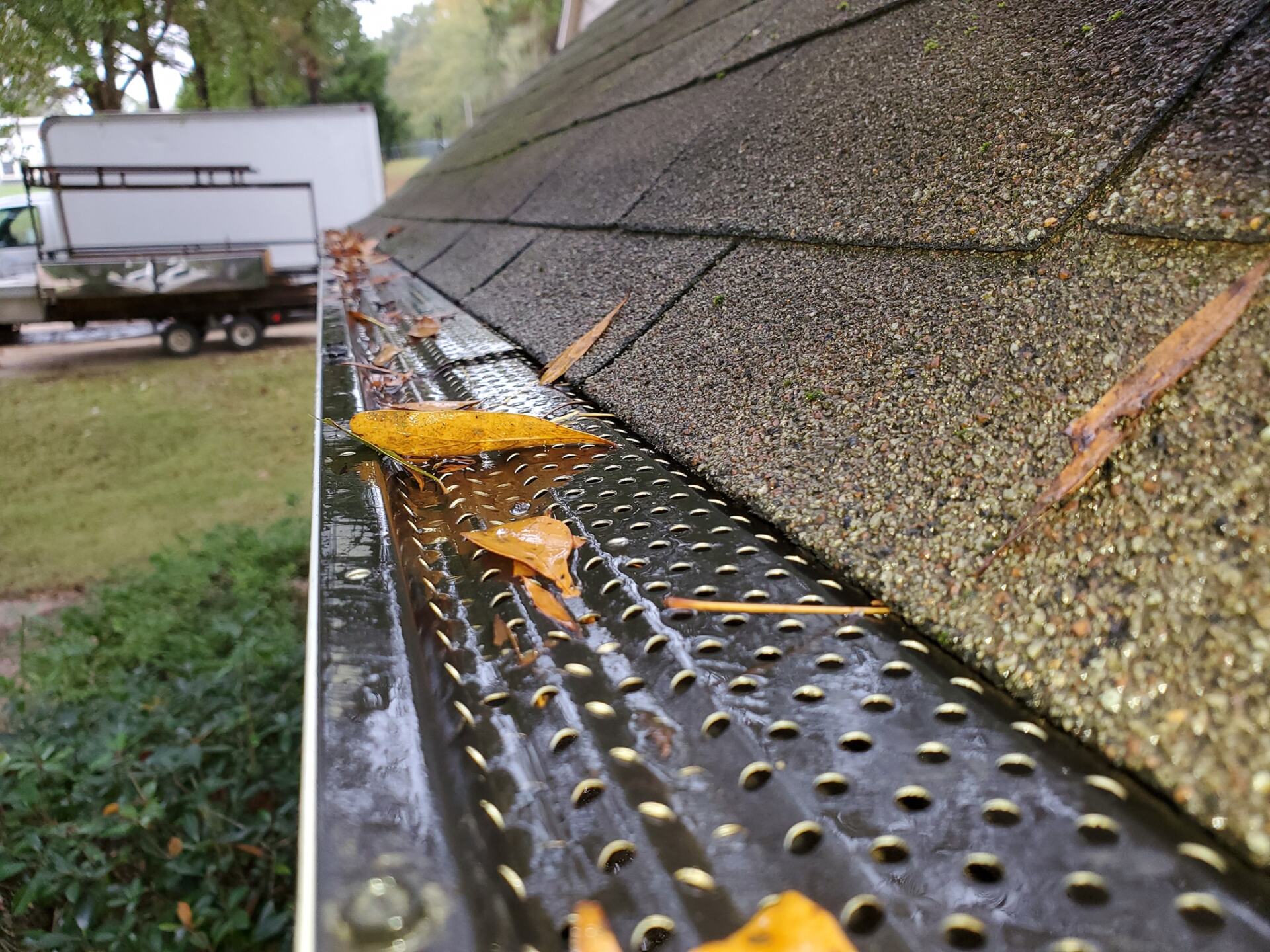 A gutter with leaves on it and a truck in the background.