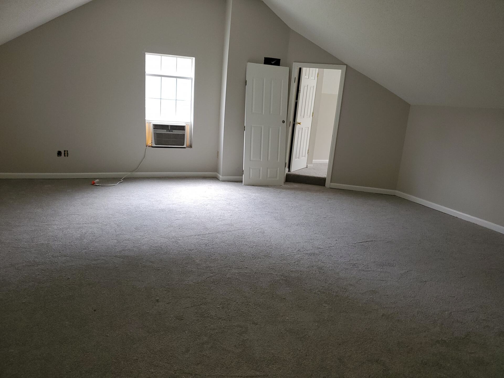 An empty room with a carpeted floor and a window.