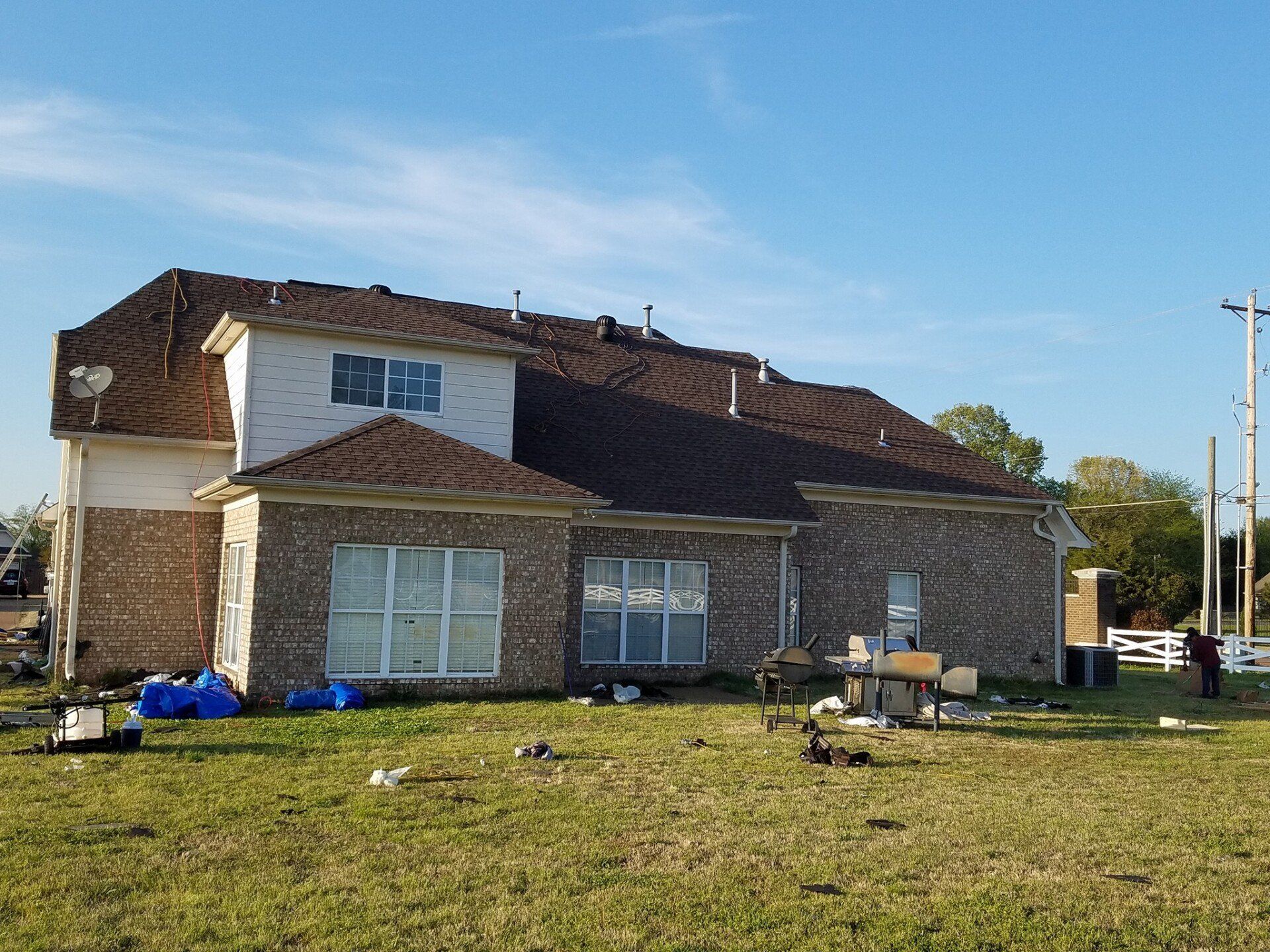 A large brick house with a brown roof is sitting in the middle of a grassy field.