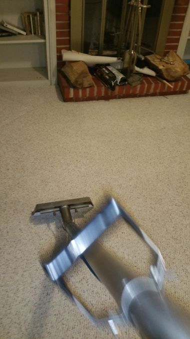 A steam cleaning wand extracts dirt from a beige carpet, leaving a clean, light-colored path behind.
