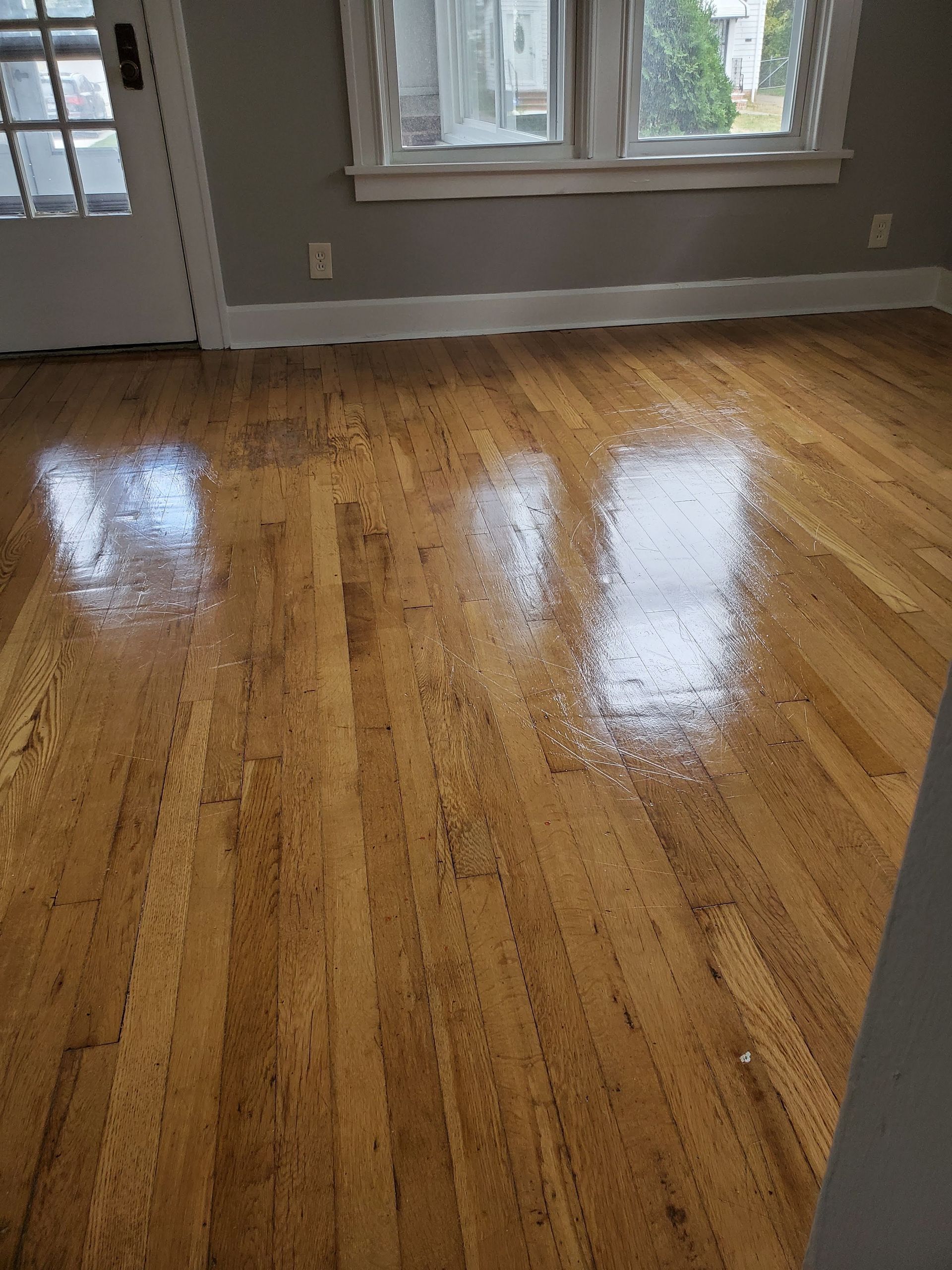 Empty room with glossy hardwood floor and a window on the far wall