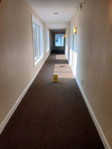 A person uses a professional carpet cleaning machine on a blue carpet in a bright, modern open-plan office.