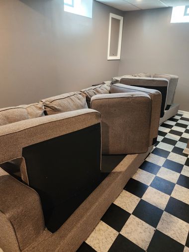 A person wearing black gloves uses a machine to deep clean a grey fabric sofa.