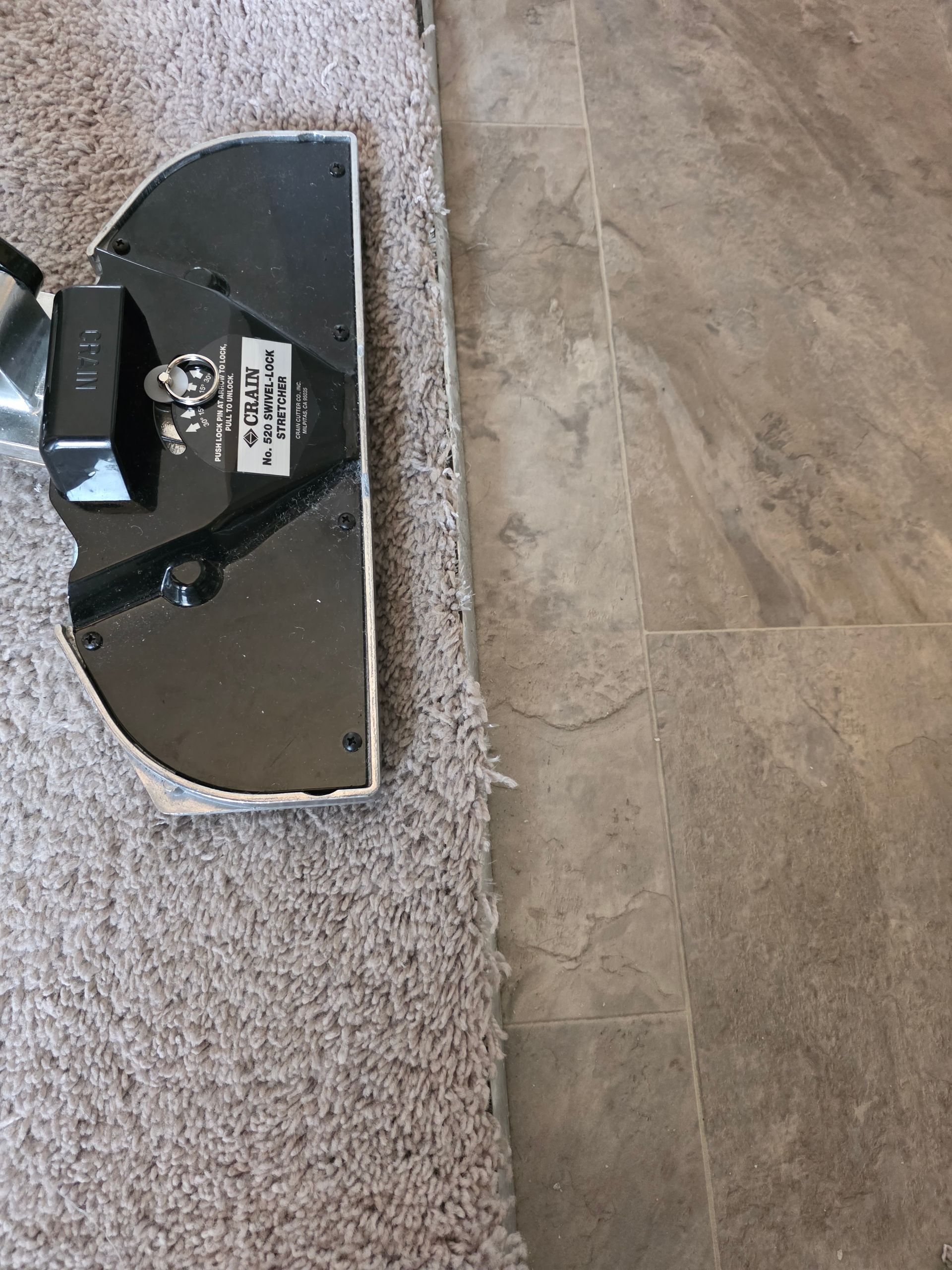 Black robotic vacuum on beige carpet beside gray tile floor.