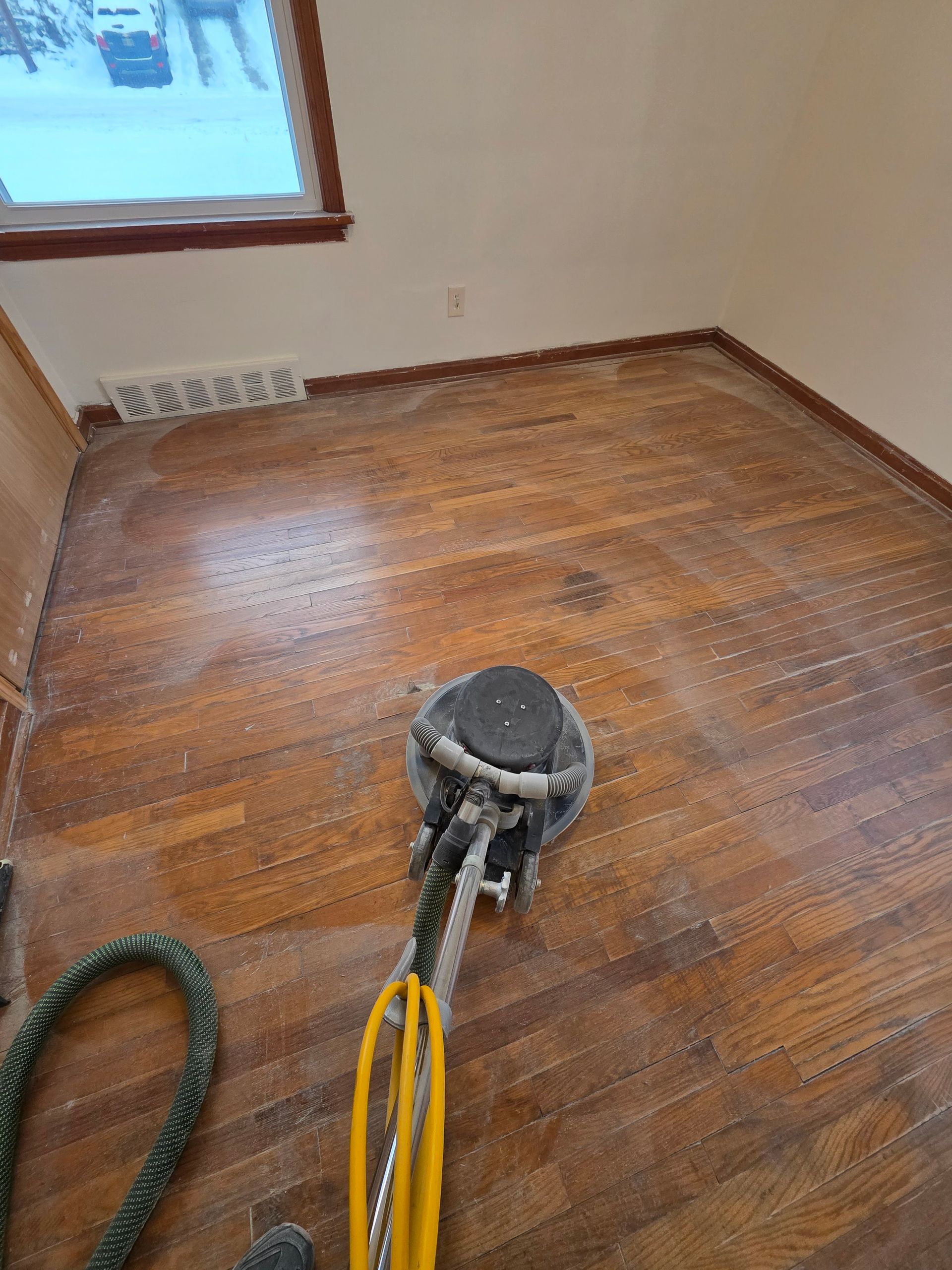 Shiny, polished hardwood floor in a well-lit hallway with a floor buffer in the background.