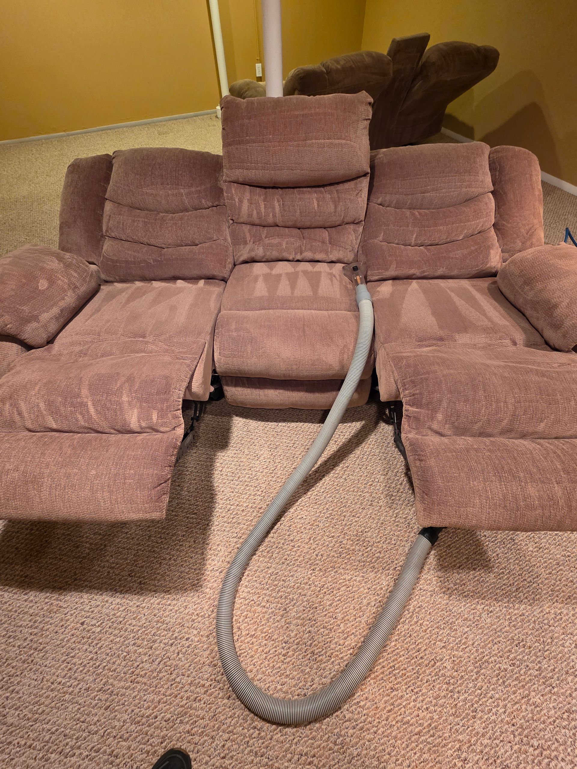 A sofa being steam cleaned, showing a clear difference in the fabric's appearance.