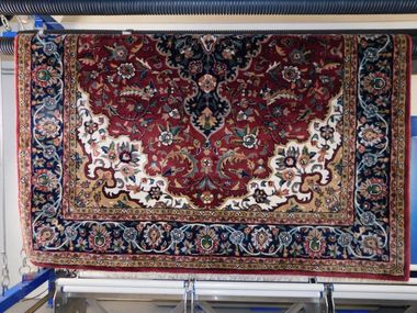A vacuum wand cleans a strip of a dark-patterned ornate rug, revealing the lighter, clean fabric beneath.