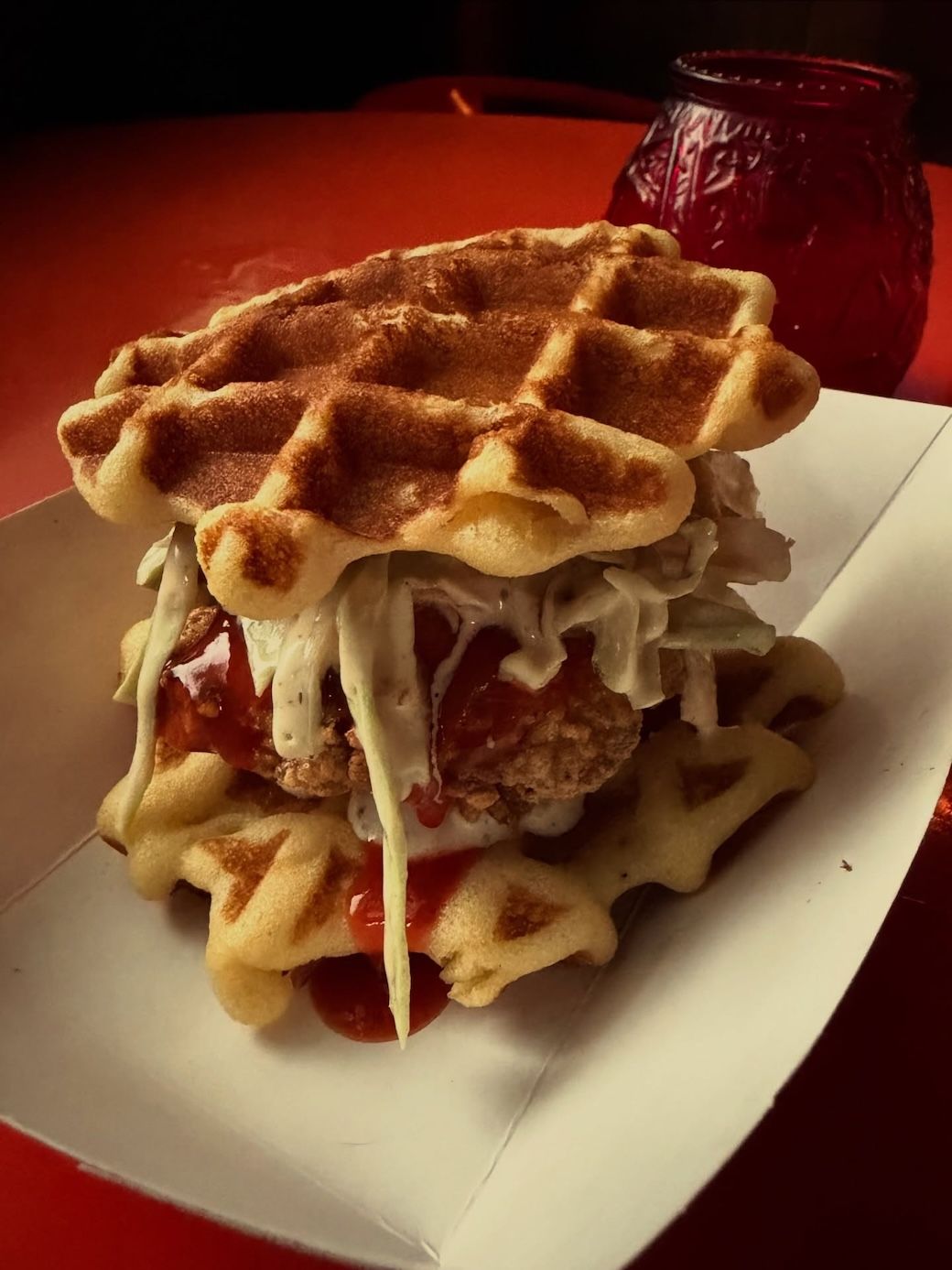 Waffle ice cream sandwich with whipped cream and strawberry sauce on a white plate