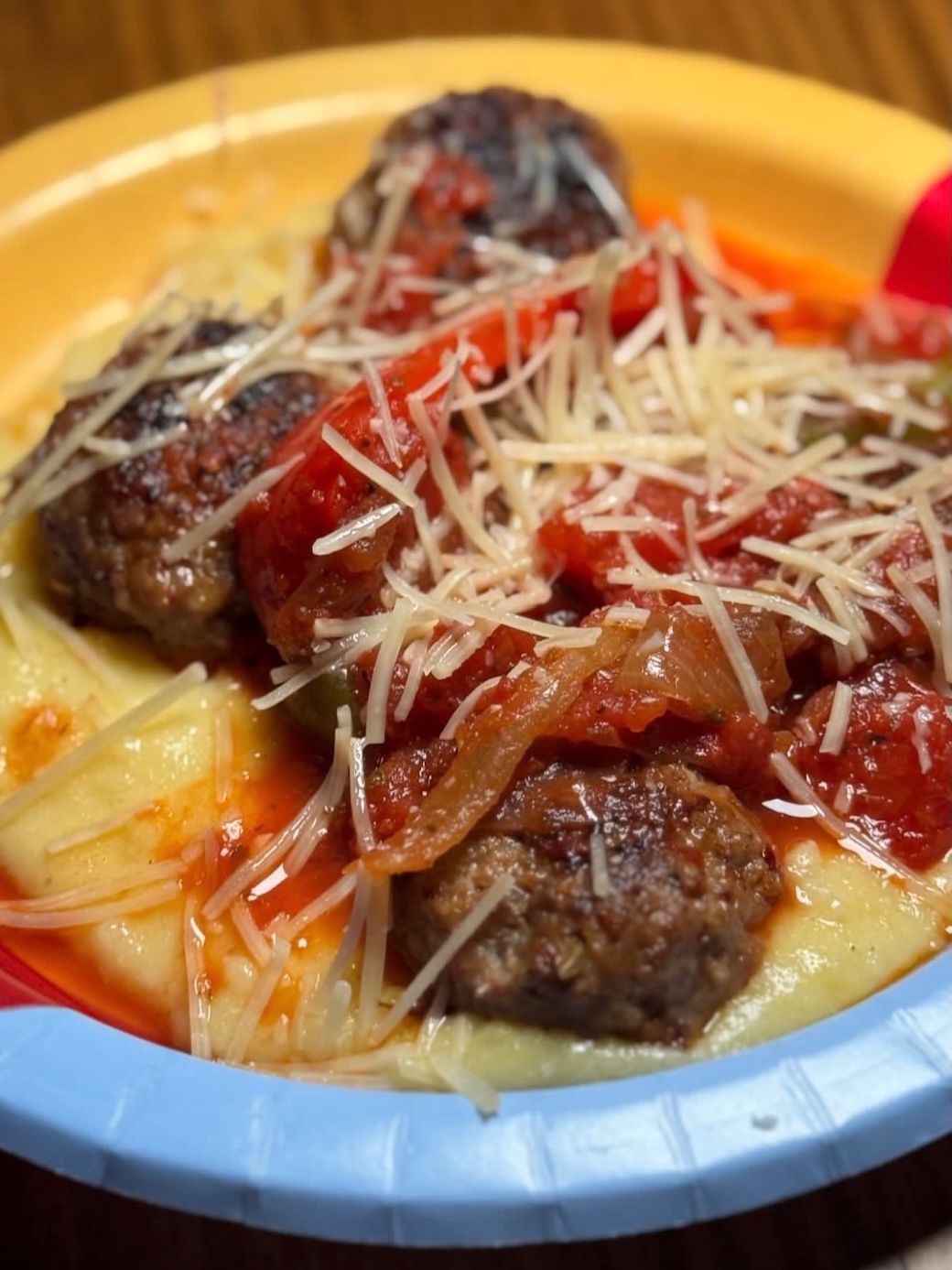 Meatballs in red sauce over creamy mashed potatoes, topped with shredded cheese in a blue bowl