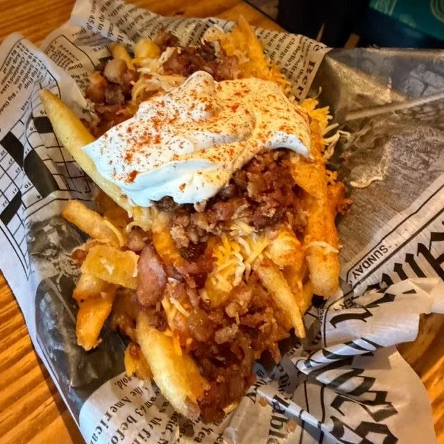 Loaded fries topped with pulled meat, sauce, and a dollop of sour cream on newspaper-style wrapping