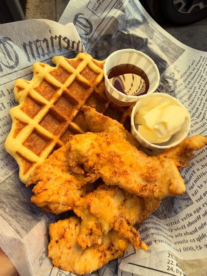 Chicken and waffles with syrup and butter on newspaper-style paper