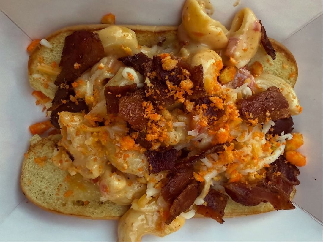 Close-up of a messy sandwich with melted cheese, bacon, and crumbs on a white plate