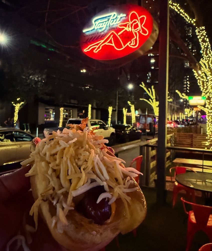 Dessert with whipped cream at a neon-lit outdoor café at night, with street reflections and chairs nearby